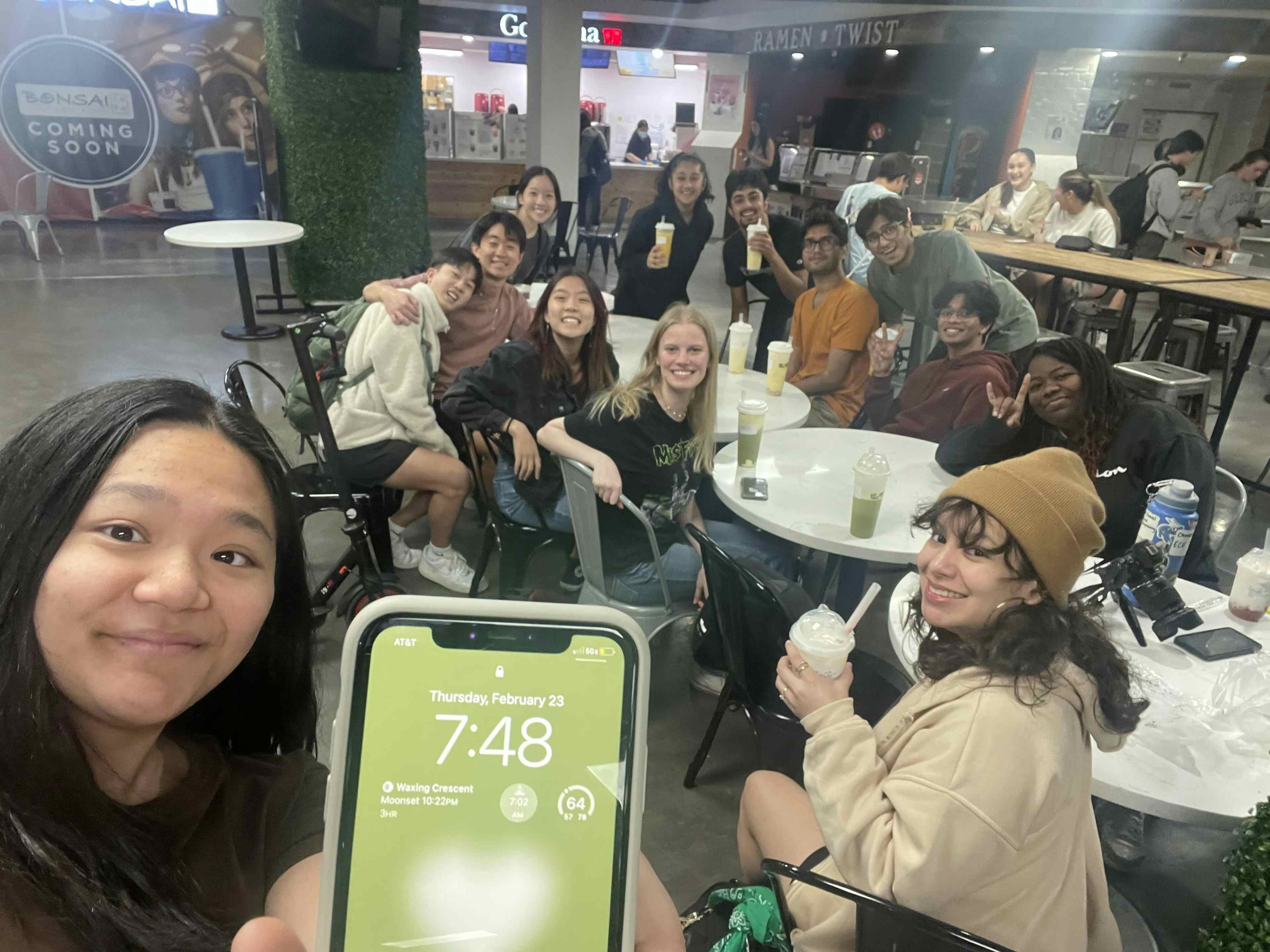 Group photo looks at camera while a member shows their phone's clock to the camera