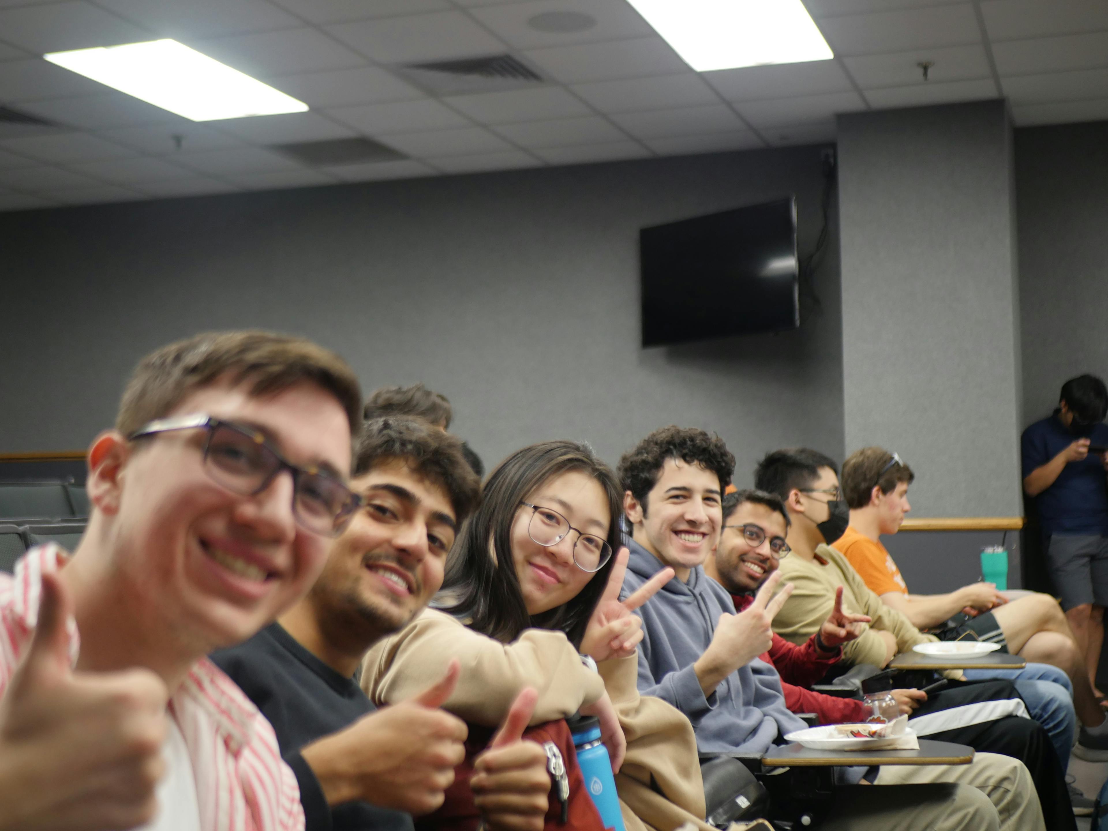 IEEE students seated in a classroom row, smiling at the camera